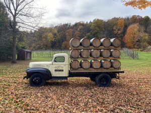 Apple cider barrels on a truck with a farm background.